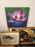 Photo showing the colorful Lotus silkscreen art with vibrant shades of purple and green, leaning on the wall above two framed cat prints.