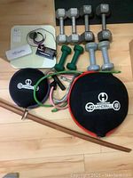 Fitness gear including various weighted dumbbells, Hyperwear Sandbell weights, resistance bands, and wooden practice katana.