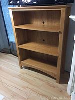 Straight-on view of wooden bookcase showing front with 3 shelves and two cable holes on back panel