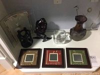Wide view of all items on white surface showing picture frames, two statues, glass cube, and vase with sun ornament.