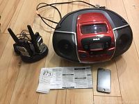 Photo showing the RCA red and black portable CD radio, two Uniden GMRS two-way radios with antennas and charging base, Apple iPod and instruction manual on wooden floor.