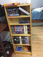 Image showing light oak wooden shelf filled with DVDs, VHS tapes, a board game, and dice.
