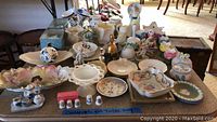 Photo showing a table filled with various art glass, ceramic decorative pieces including bowls, plates, thimbles, and figurines arranged closely together.