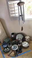 View of entire lot showing pottery, marble tray, wind chime and triangle instrument grouped together on floor and hanging in corner