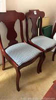 View of two wooden dining chairs with curved backs and upholstered seats with blue and white scallop fabric.