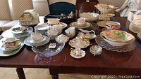 Wide view of the full assortment of ceramic dishes, cups, saucers, bowls, and serving pieces arranged on wooden table.