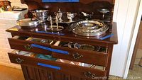 Overview of silver-plated items arranged on wooden cabinet shelves and drawers