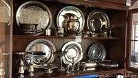 Two-shelf display showing multiple round platters, pitcher on top shelf and servers on lower shelf.