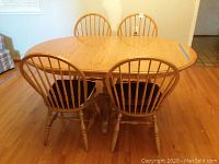 Wooden dining table with four matching spindle-back chairs shown from side angle, displaying the table top and chair backs.