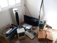 Corner of room showing Visio flatscreen TV, Canon Pixma scanner, Apple Macintosh SE computer, keyboard, tower fan, wicker chair, photo albums and documents in containers.