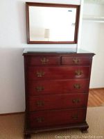 Full view of the wooden dresser with glass top and brass handles, with the mirror hanging above it on the wall