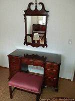 Full view of desk with attached custom glass top, mirror above it, and stool in front