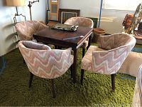 Image showing the square wooden dining table surrounded by four pastel patterned upholstered chairs on a green shag carpet.