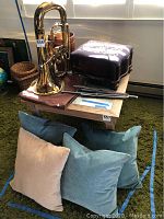 Wide angle photo showing brass euphonium, footstool, music stand parts and four pillows on green carpet