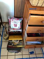 Wide view showing open drawers filled with folded fabric pieces, thread spools on top of drawers and a pincushion, with metal boxes and other sewing supplies.