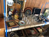 Full view of bar counter with items: bar lamp, stained glass window, glassware, trays, lantern, framed plaque, coasters, ashtrays, and drawers with cords and bar tools.
