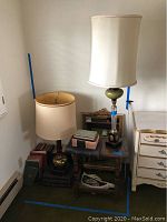 Two table lamps on and beside a small wooden side table with books underneath. Wall background.