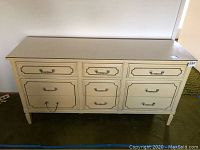 Front view of cream-colored dresser with nine drawers and metal handles, one handle missing on a drawer.