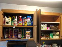 Front view of two open wooden cabinets with multiple bottles and containers of gardening products including bug sprays, pesticides, and plant food.