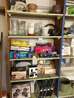 Full shelf view of kitchen items including food wraps, boxes, pasta machine, serving dishes