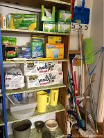 Photo of five shelves holding cleaning and picnic products, including Swiffer items, Scotch Brite sponges, napkins, pitchers, mops, brooms, and dustpans.