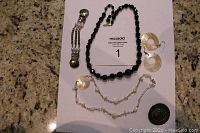 Photo showing entire lot of vintage jewelry with black glass beaded necklace, shell earrings, sweater clip, shell and bead necklace, and silver pin.
