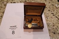 Photo showing three sets of cufflinks and one Canadian forces pin inside a brown box on a countertop.