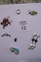 All jewelry items spread on a white background with auction card, showing ring, multiple pairs of earrings, pendant.