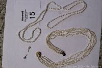 Image showing long single-strand freshwater pearl necklace above and vintage multi-strand freshwater pearl necklace with gold-tone clasp below along with pair of pearl stud earrings on a white sheet with lot number.
