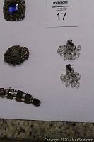 Top view of four vintage jewelry pieces arranged on white paper with number 17 label, showing antique brooches, crystal bead earrings, and bracelet.