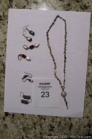 Full view of long silver chain necklace with a pearl inset along with four pairs of artisanal earrings on card