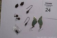 Six pairs of varied silver wired earrings laid on white background, including inlaid stone long dangle, small stud earrings, and black pearl studs; shows variety and condition.