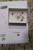 Pair of amethyst stud earrings and matching sterling silver pendant chain presented in a jewelry box and arranged on auction sheet.