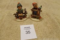 Two Goebel Hummel figurines on carpet with auction number card in front.