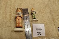 Two choir singer figurines with ruler for size reference on beige background.