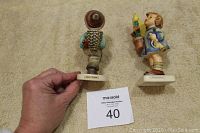 Photo of both figurines side by side showing front view, titles on bases, and overall size relative to hand.