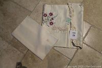 Photo showing the folded tablecloth with embroidered rose design and two cream napkins.
