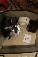 Photo showing black smooth leather belt, white leather belt with holes, and a large decorative metal buckle belt.