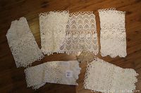 Top view showing five different vintage lace café curtains with intricate patterns spread on wooden floor.