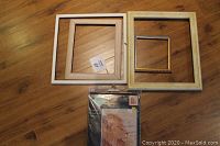 Four wooden frames and one packaged cross-stitch lion pattern kit on wooden floor.