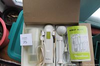 Top-down photo of Moulinex multi mixer components including the main unit, attachments, measuring cup, and manual inside the original box, on a teal surface near a window with potted plants nearby.