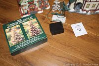 Overview of two Christmas houses, the boxed set of Avon tree-shaped cookie cutters, small Christmas tree, lighting and black battery pack on wooden surface.