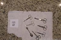 Seven small vintage sewing/needlework scissors laid out on kitchen counter with one small sterling spoon