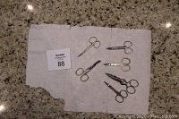 Six vintage stainless steel scissors on a white cloth showing various sizes and styles, including straight and curved blades, some marked Solingen Germany and Realmont 2008.