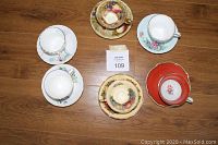 Overhead photo showing five bone china tea cups with matching saucers arranged in a circle on wood floor