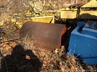 Image showing the large steel roller with rusted outer surface and red painted ends, surrounded by dry leaves and farm equipment.