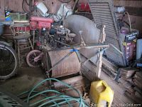 Dirt packer, gas-powered with visible rust and soil, situated in a cluttered storage space with other items nearby.