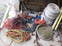 Wide view of multiple coiled hoses and extension cords placed on the ground outside, including industrial water hoses and extension cords in various colors.