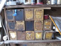 Photo showing 14 vintage metal storage boxes stacked in a 4x4 configuration with some missing boxes, all displaying signs of rust and soil.
