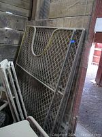 Steel fence panels with diamond mesh and U-shaped design leaning against a wooden wall.